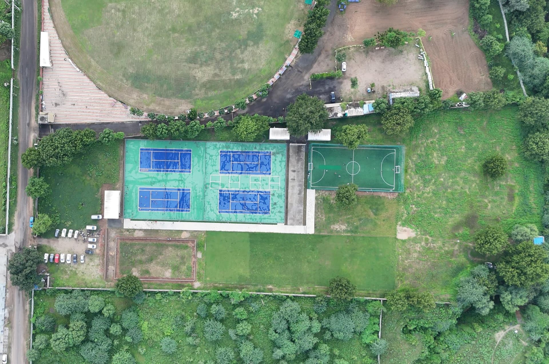 Aerial view of Drona Sports Academy's tennis courts, turf ground, and open garden